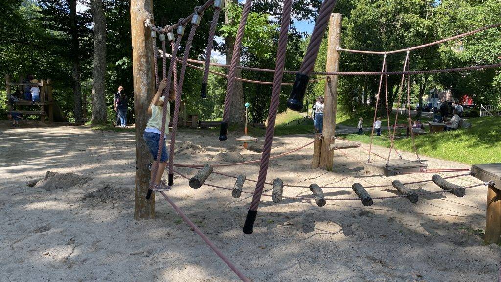 Kind am Seil-Balancierparcours aus dicken Tauen und Baumstämmen im Sandbereich des Spielplatzes Räuberberg in Bad Wildbad