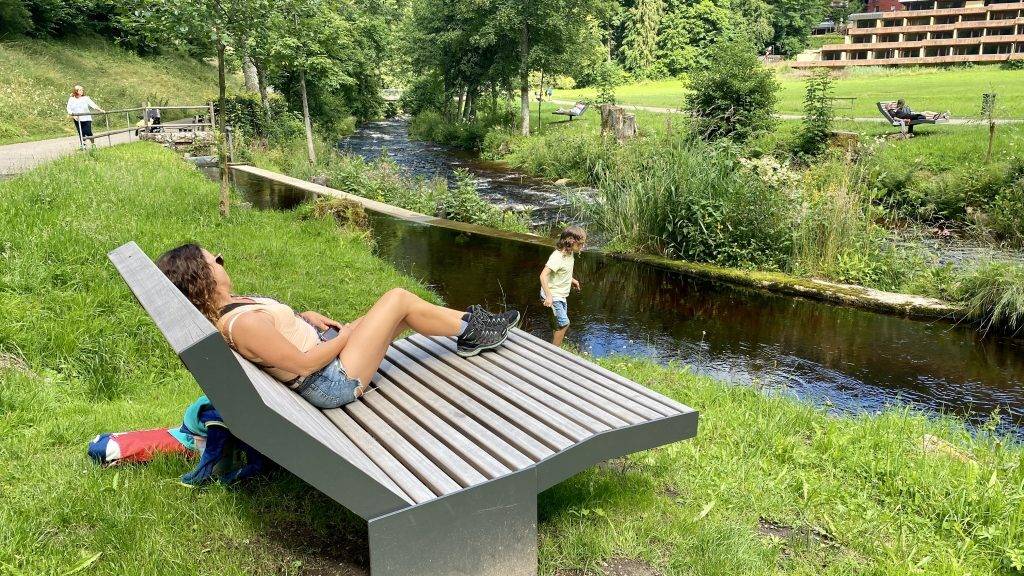 Frau liegt auf einer Himmelsliege an der Enz im Kurpark Bad Wildbad, im Hintergrund steht ein Kind am Wasser