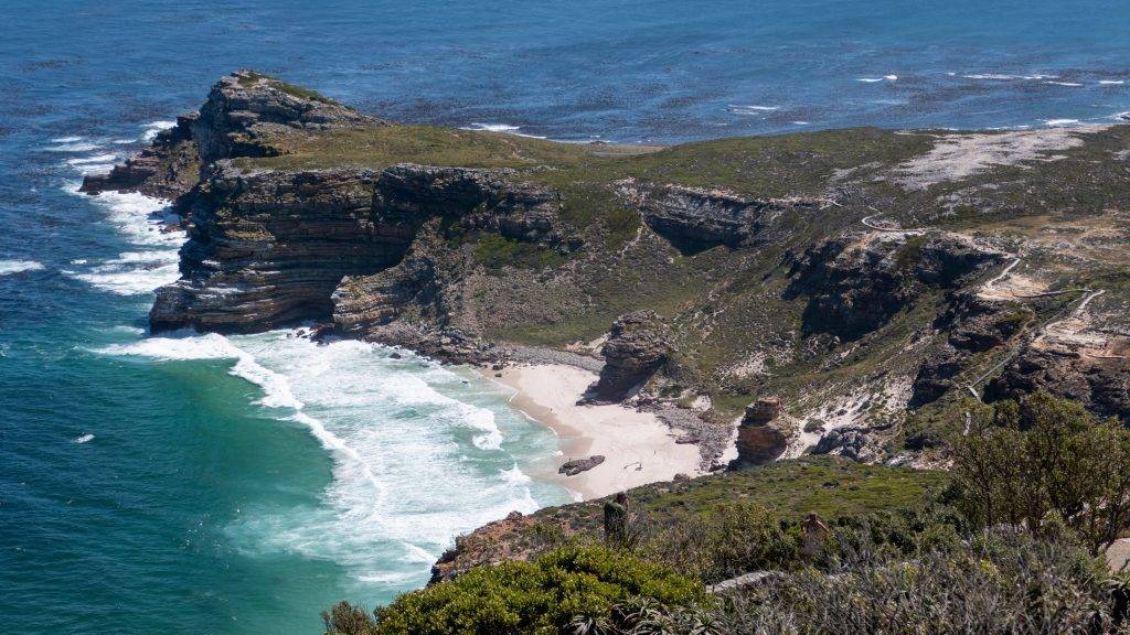 Fernblick auf den Dias Strand mit der Brandung eingerahmt von Felsen