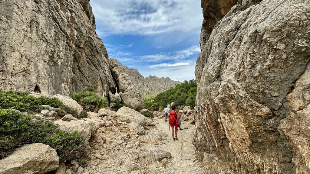 Eine kleine Wandergruppe geht zwischen zwei riesigen Felswänden hindurch auf einem steinigen Weg.