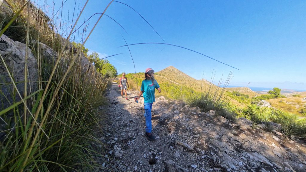 Wandern mit Kindern auf schmalen, steinigen Pfaden in einer hügeligen Landschaft mit Blick auf das Meer