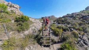 Frau klettert über ein Gatter auf einer Wanderung im Nationalpark Llevant auf Mallorca, begleitet von Familie