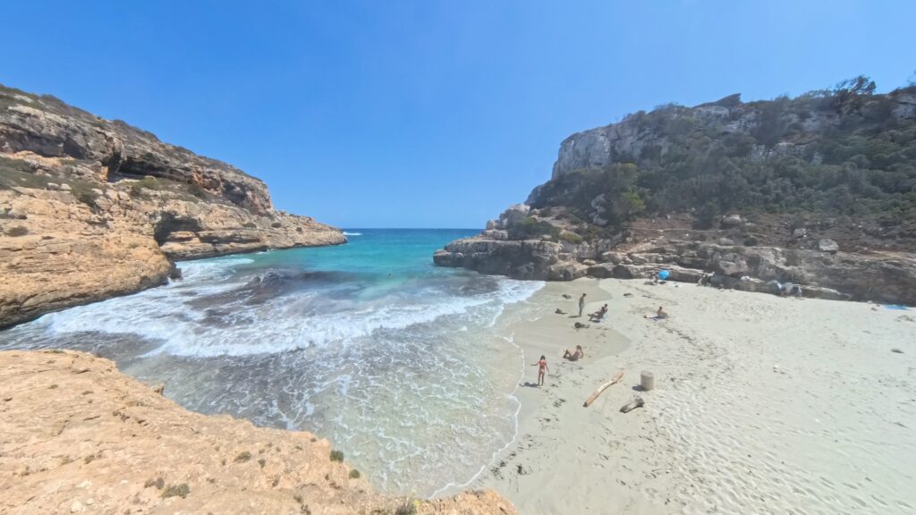 hohe Wellen rauschen in die kleine, abgelegene Bucht mit großen Sandstrand, eingerahmt von Steinhügel