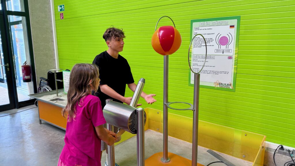 Kinder die den Ball im Luftstrom versuchen durch zwei runde Kreise zu bewegen