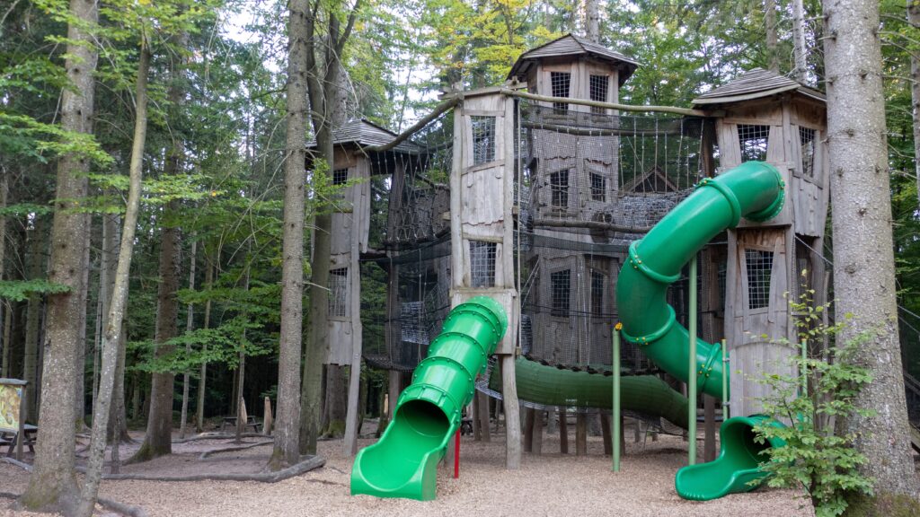 Großes Klettergerüst mit Holztürmen, Netzen und zwei grünen Röhrenrutschen im Abenteuerwald Bad Wildbad
