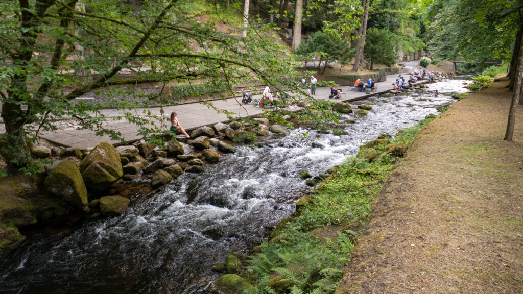 Familien sitzen auf Steinen und auf der Uferterrasse an der Enz im Kurpark Bad Wildbad, im Wasser kleine Stromschnellen