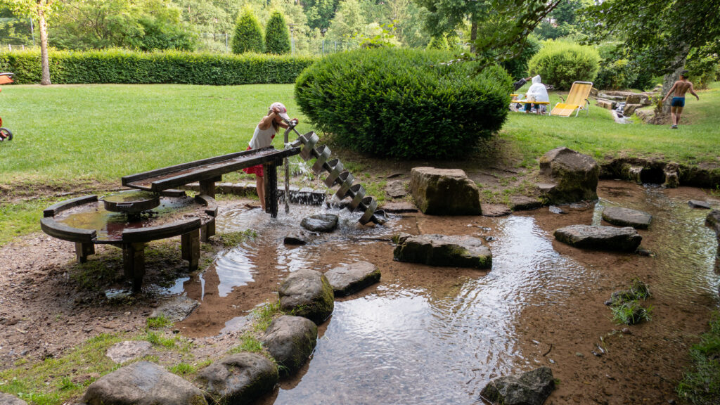 Kind dreht die Archimedische Spirale am Matschplatz im Kurpark Bad Wildbad, das Wasser läuft über die Holzrinne