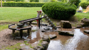 Mädchen bedient die Archimedische Spirale am Wasserspielplatz im Kurpark Bad Wildbad, das Wasser läuft in den Bachlauf