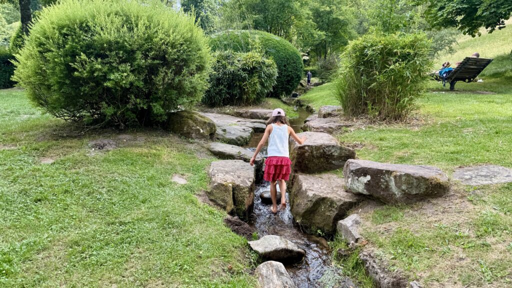 Kind läuft barfuß über die Steine im Bachlauf neben dem Matschplatz im Kurpark Bad Wildbad