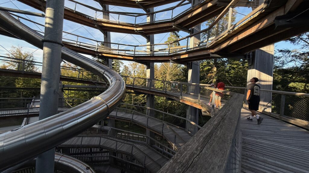 Spiralförmige Holzrampen im Inneren des Aussichtsturms mit der Rutschenröhre daneben